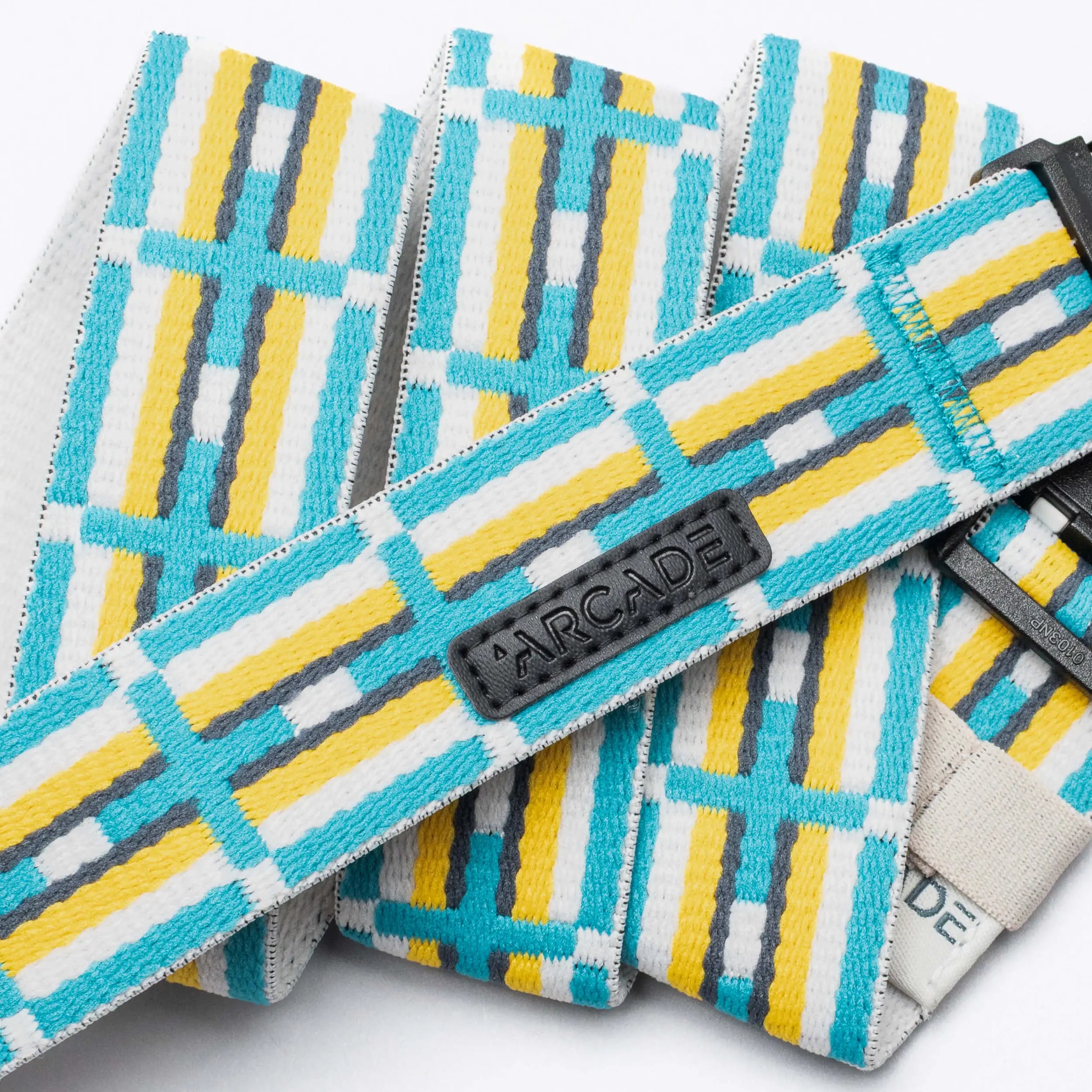 A close-up of the Vernan Kee belt by Arcade Belts, featuring yellow, white, turquoise, and gray geometric patterns inspired by Navajo rugs. A black patch displays the Arcade Belts logo in raised letters.