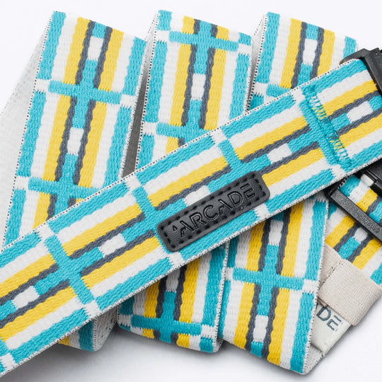 A close-up of the Vernan Kee belt by Arcade Belts, featuring yellow, white, turquoise, and gray geometric patterns inspired by Navajo rugs. A black patch displays the Arcade Belts logo in raised letters.