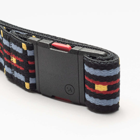 The Vernan Kee belt by Arcade Belts features a geometric pattern in red, yellow, and blue on black elastic with a durable black plastic buckle—ideal for travel or daily wear.
