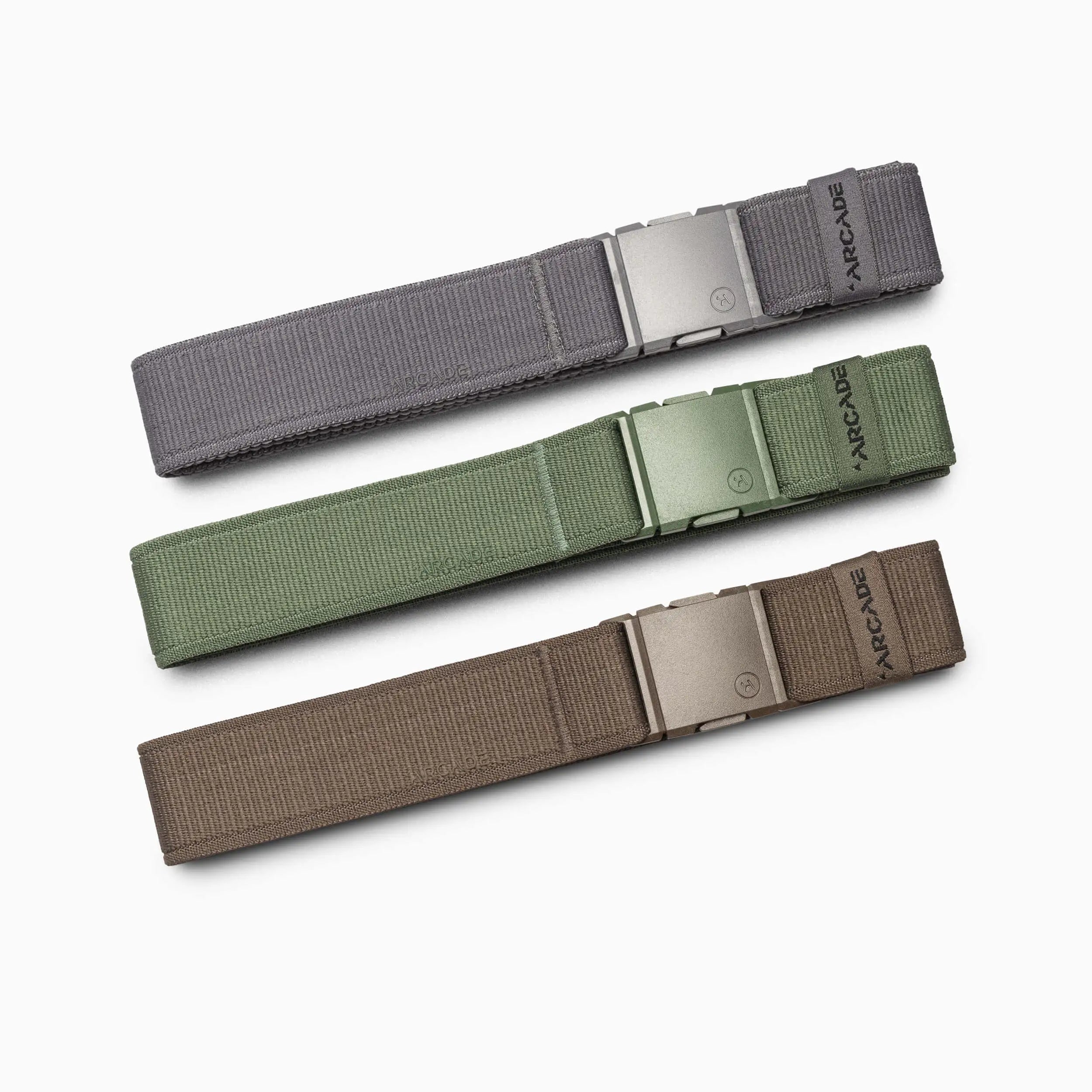 Three Atlas Terrain Kit fabric belts by Arcade Belts—in gray, olive green, and brown with natural textures—are arranged parallel on a white background. Each features a rectangular metal buckle and the Arcade Belts name at the strap end.