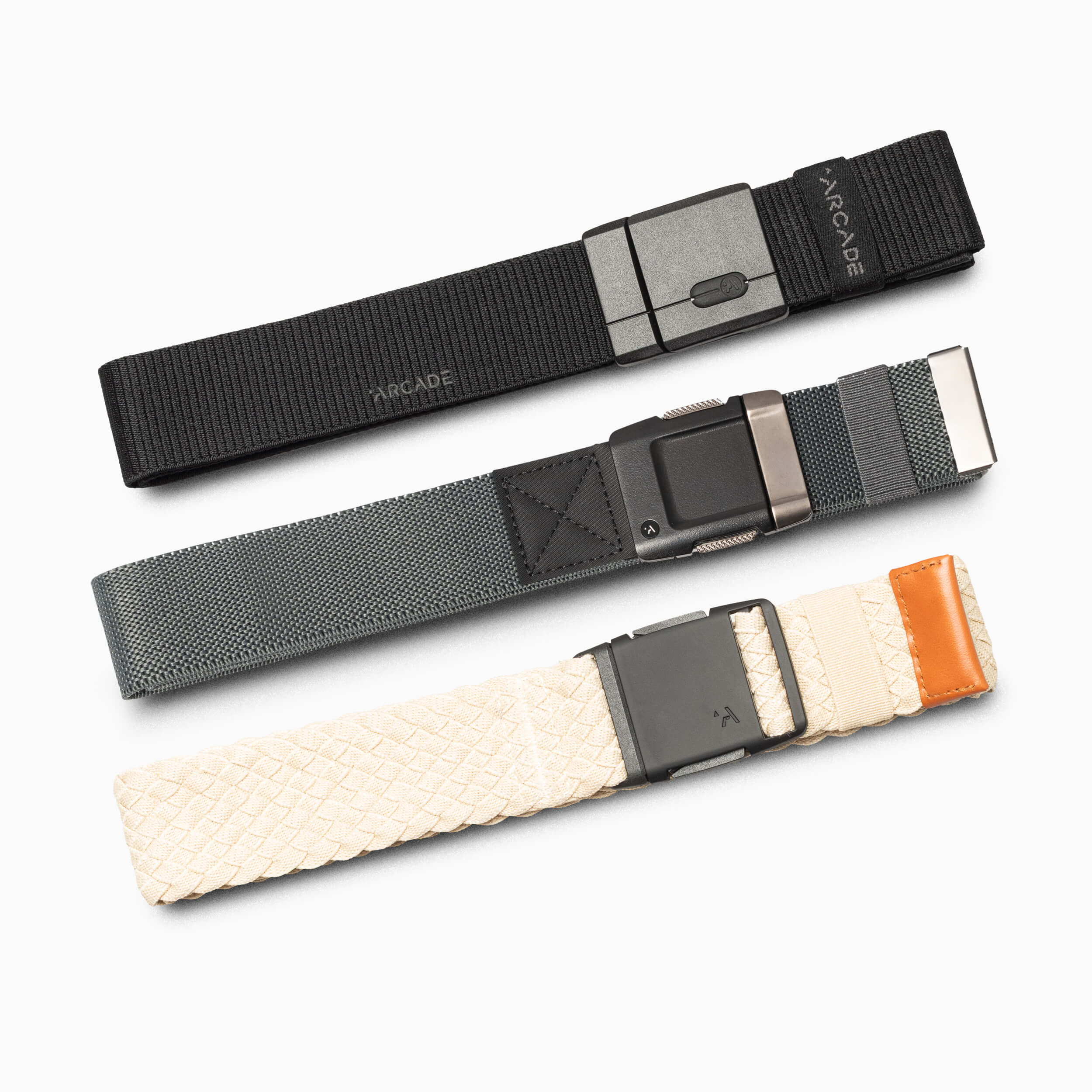 The Arcade Belts Golf Kit displays three casual belts on a white background: a black lightweight woven flex belt, a gray belt with a magnetic buckle, and a cream woven belt with brown leather near the buckle.