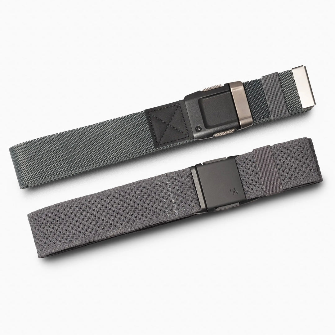 Two gray Arcade Belts from the Lifestyle Kit, both with black metal buckles, are parallel on a white background; one is smooth and the other has a textured mesh-like pattern—ideal travel belts for comfort and style.