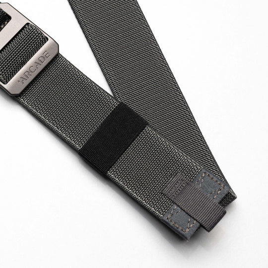 A close-up of the Arcade Belts Hardware Belt Loopkeepers: a grey stretch webbing belt with reinforced stitching and a black metal buckle labeled ARCADE, shown on a white background—ideal for versatile travel wear.
