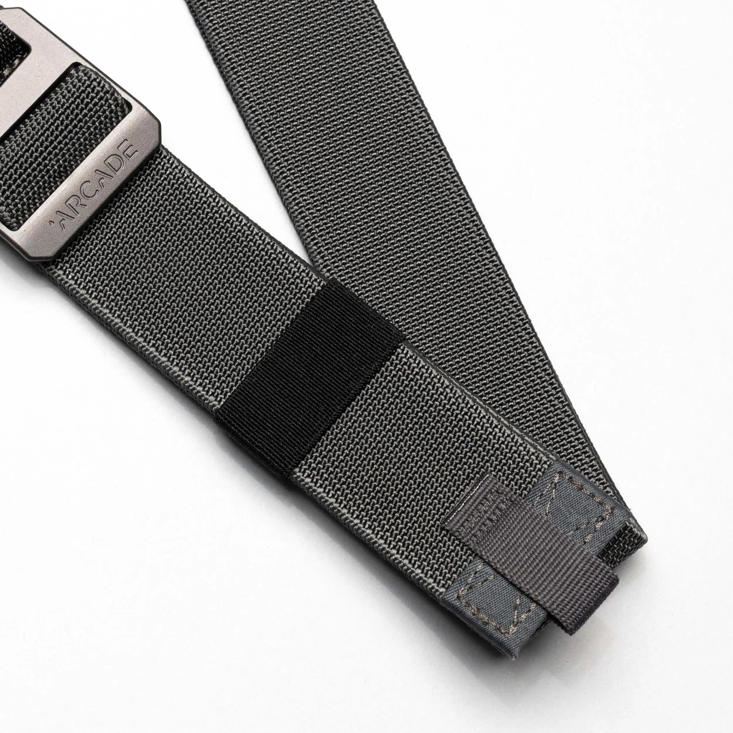 A close-up of the Arcade Belts Hardware Belt Loopkeepers: a grey stretch webbing belt with reinforced stitching and a black metal buckle labeled ARCADE, shown on a white background—ideal for versatile travel wear.