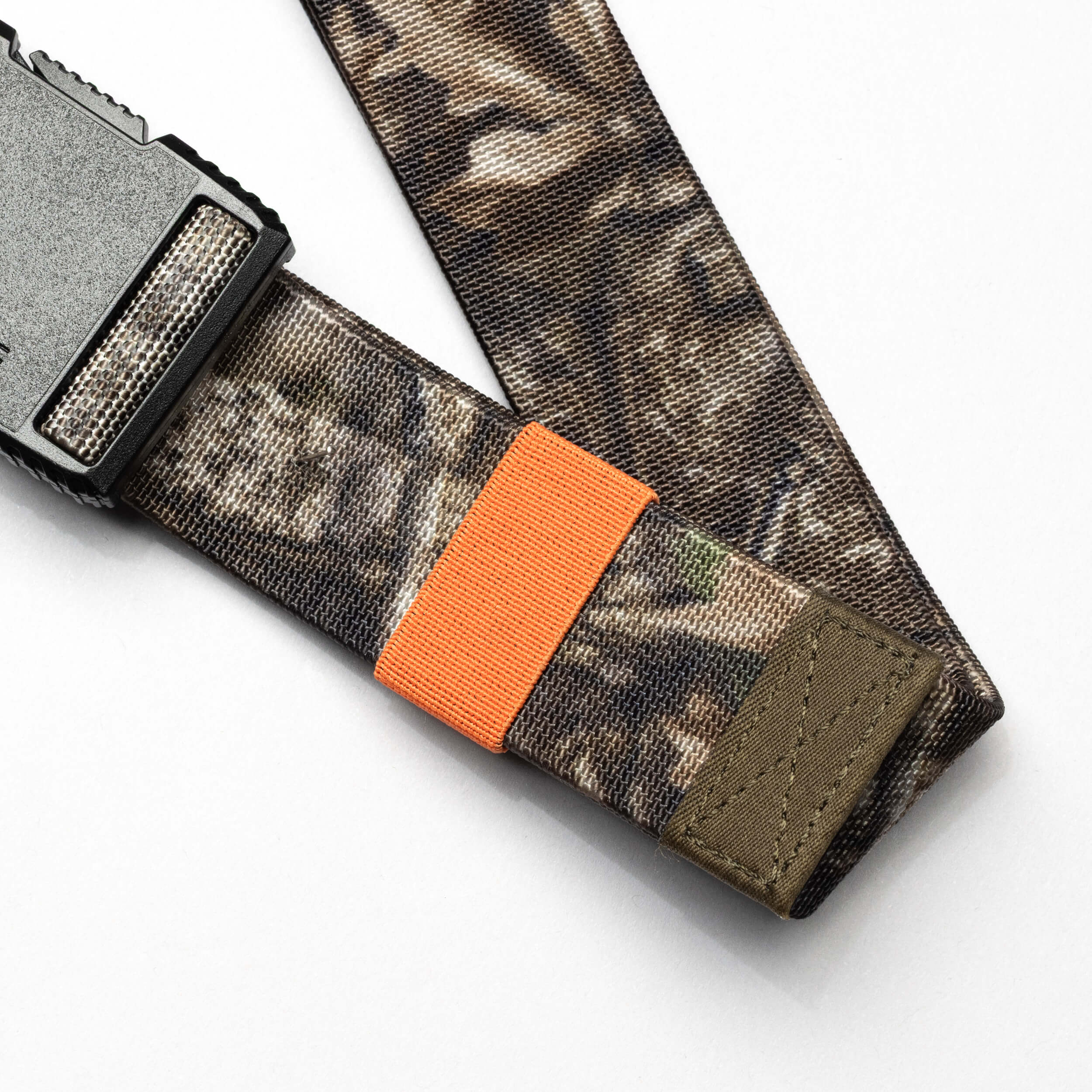 The Arcade Belts Hardware Belt Loopkeepers features a camouflage pattern, elastic stretch for comfort, a plastic buckle, and an orange loop, displayed on a white surface.