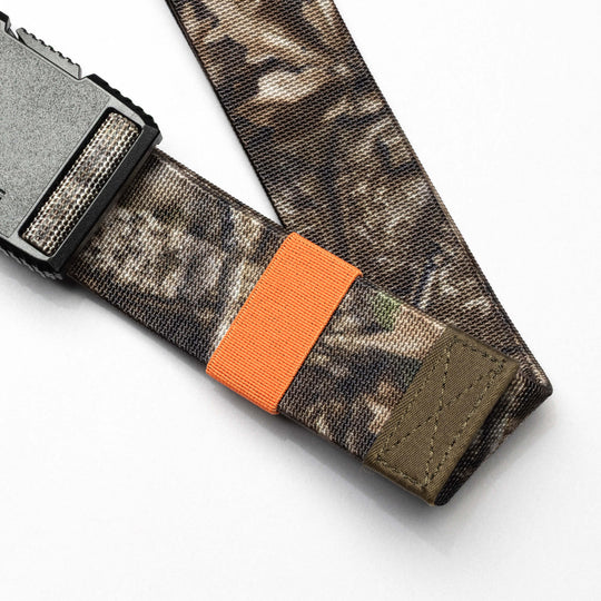 The Arcade Belts Hardware Belt Loopkeepers features a camouflage pattern, elastic stretch for comfort, a plastic buckle, and an orange loop, displayed on a white surface.