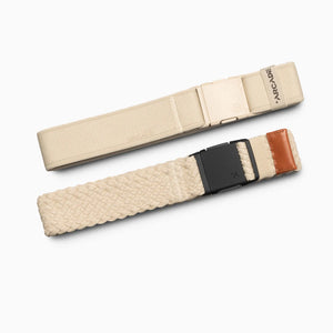 Two beige Arcade Belts Lunar Kit on a white background. The top has a smooth texture with a plastic buckle, while the bottom is an elastic stretch belt with woven texture, black buckle, and brown leather accent.