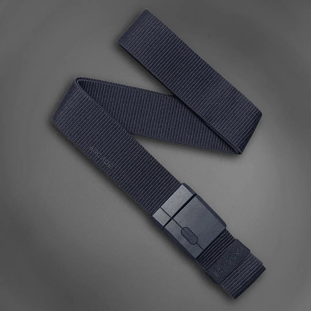 A black, ribbed nylon belt with a rectangular, matte black buckle is displayed on a gray background. The belt is partially coiled, showing its texture and modern design.