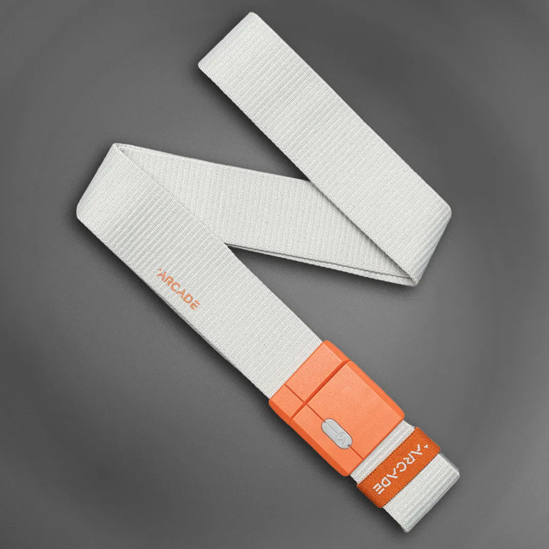 A white fabric belt with an orange plastic buckle and the word ARCADE printed near the buckle, displayed on a dark gray background.