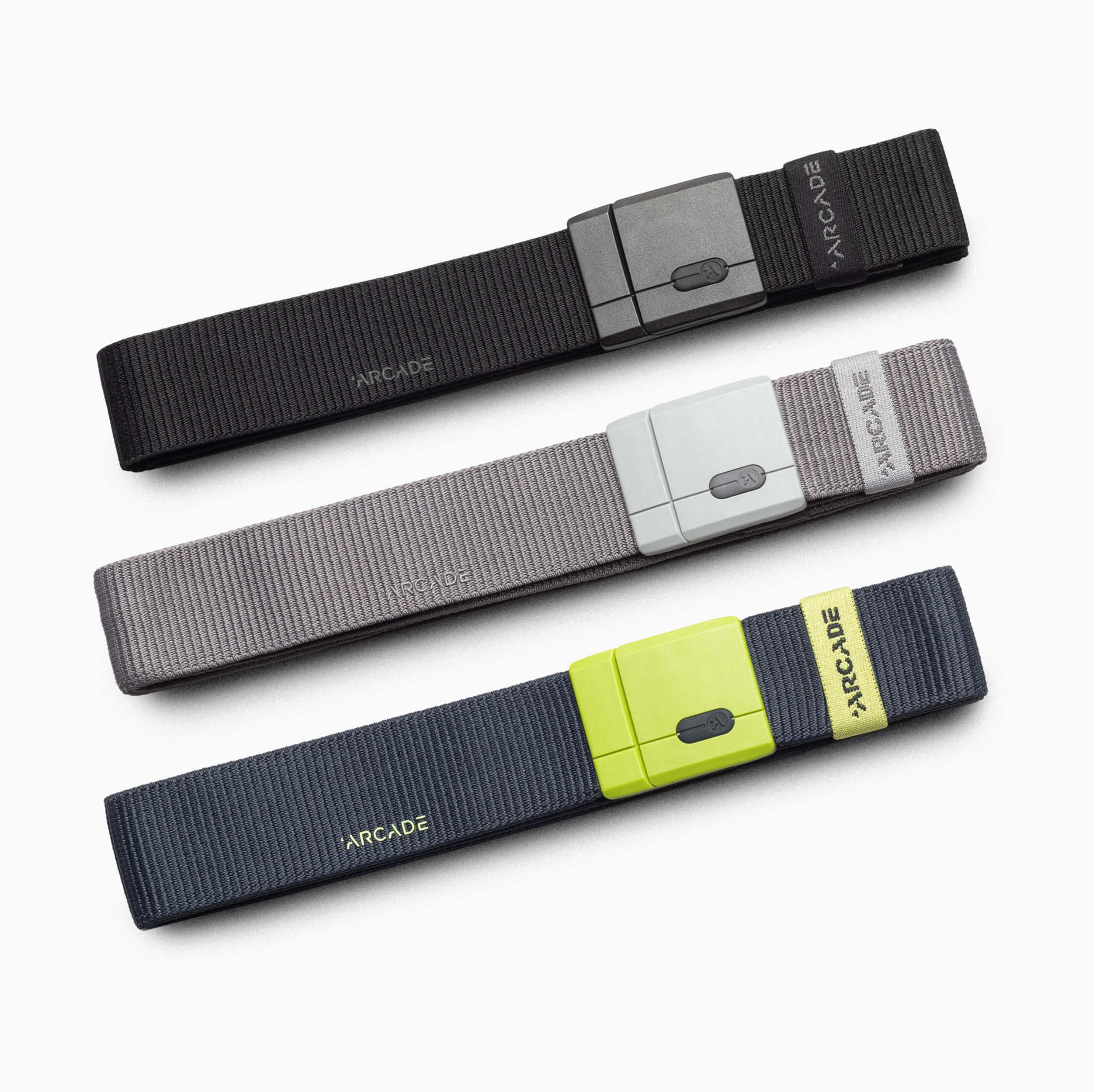Three Arcade brand web belt stretchers in black, gray, and navy blue, arranged diagonally on a clean white background.