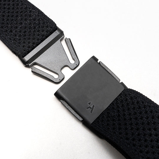 Close-up of the Arcade Belts Momentum Kit, a black Elastic Stretch Belt with a modern rectangular magnetic buckle, shown partially unfastened on a light gray surface.