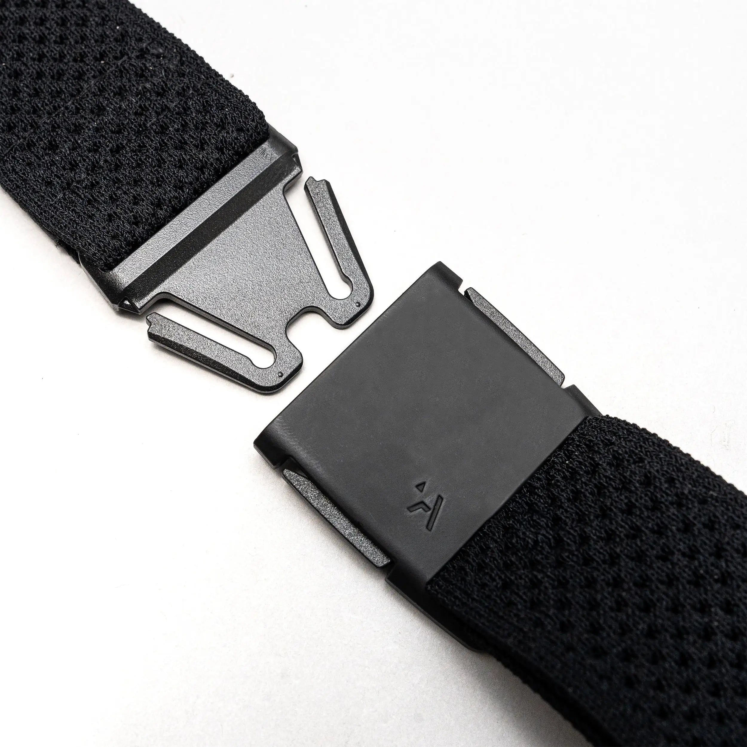 Close-up of the Arcade Belts Momentum Kit, a black Elastic Stretch Belt with a modern rectangular magnetic buckle, shown partially unfastened on a light gray surface.