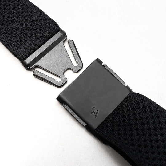 Close-up of the Arcade Belts Momentum Kit, a black Elastic Stretch Belt with a modern rectangular magnetic buckle, shown partially unfastened on a light gray surface.