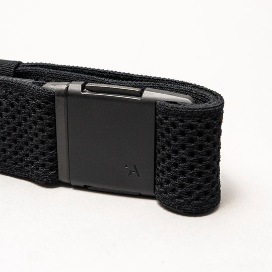 A close-up of the Arcade Belts Momentum strap in black shows its textured, mesh-like webbing and a matte black rectangular buckle with a small logo, all displayed against a light gray background.