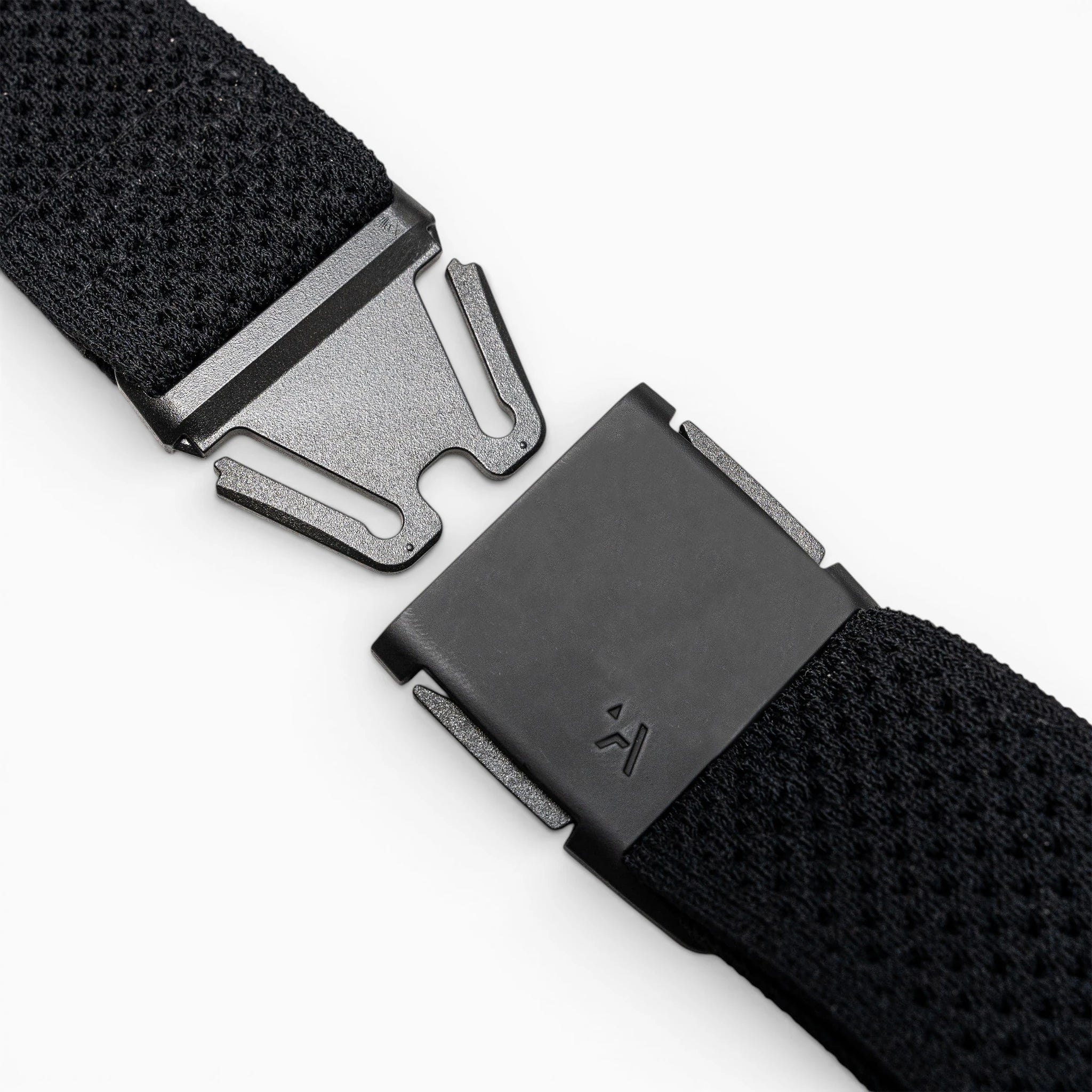 Close-up of the Arcade Belts Momentum Kit, a black Elastic Stretch Belt with a modern rectangular magnetic buckle, shown partially unfastened on a light gray surface.