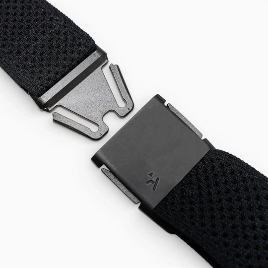 Close-up of the Arcade Belts Momentum Kit, a black Elastic Stretch Belt with a modern rectangular magnetic buckle, shown partially unfastened on a light gray surface.