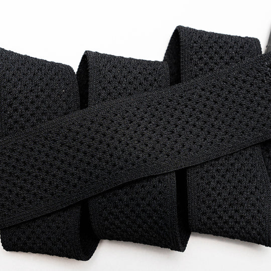 Close-up of the black Momentum elastic stretch belt by Arcade Belts, featuring a mesh-like texture and folded in a zigzag shape against a white background.