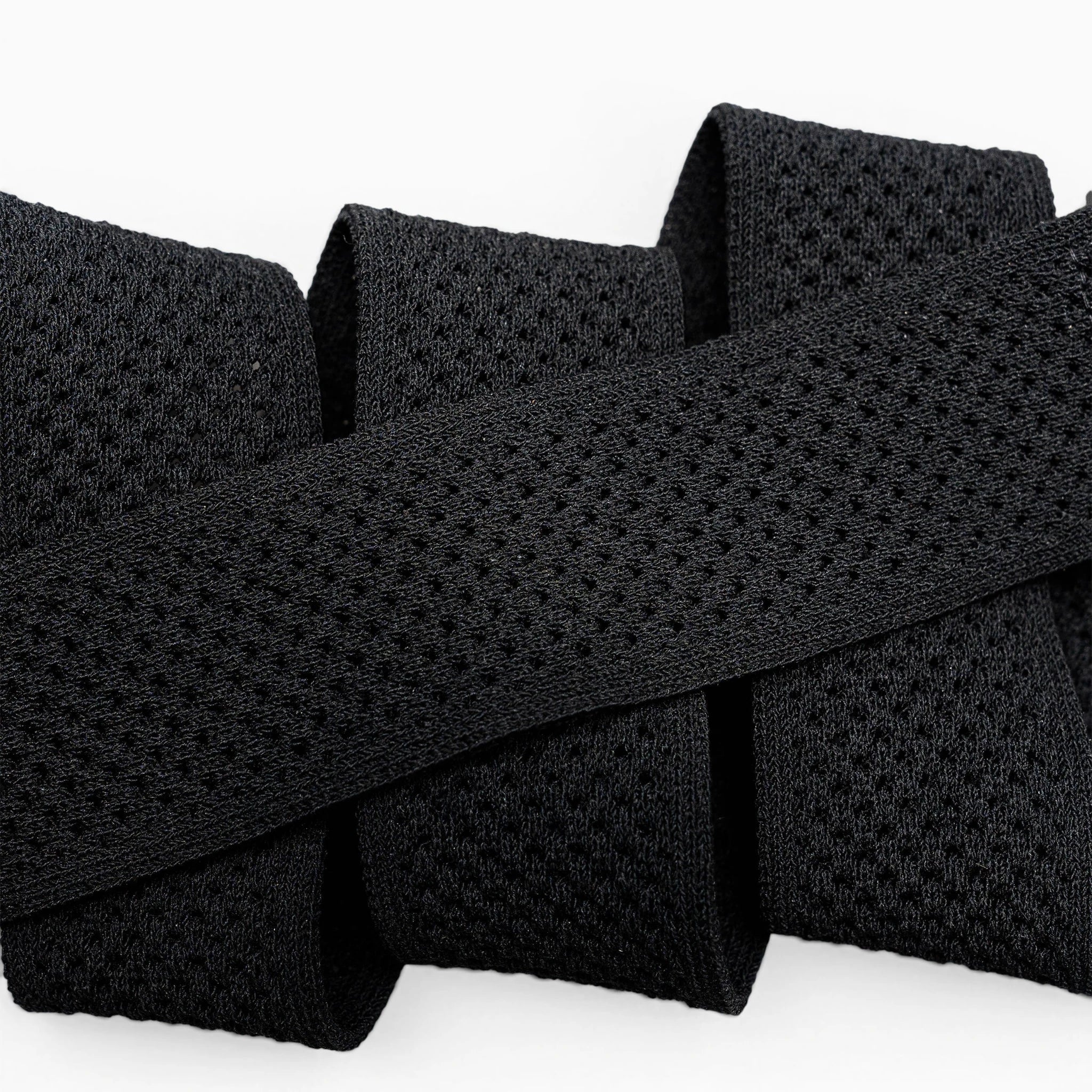 Close-up of the black Momentum elastic stretch belt by Arcade Belts, featuring a mesh-like texture and folded in a zigzag shape against a white background.