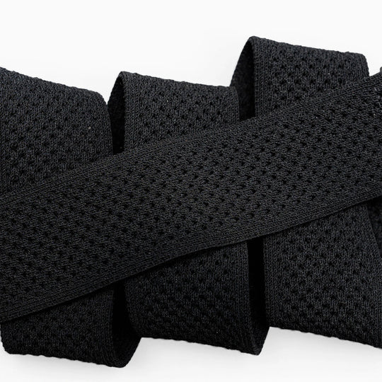Close-up of the black Momentum elastic stretch belt by Arcade Belts, featuring a mesh-like texture and folded in a zigzag shape against a white background.