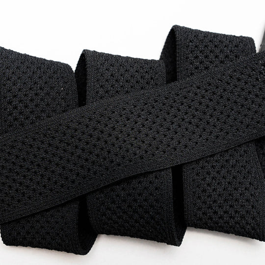 Close-up of the black Momentum elastic stretch belt by Arcade Belts, featuring a mesh-like texture and folded in a zigzag shape against a white background.