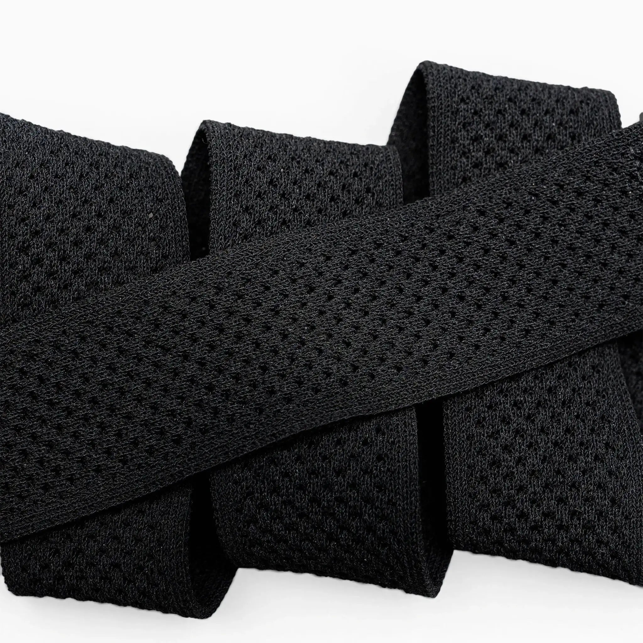 Close-up of the black Momentum elastic stretch belt by Arcade Belts, featuring a mesh-like texture and folded in a zigzag shape against a white background.
