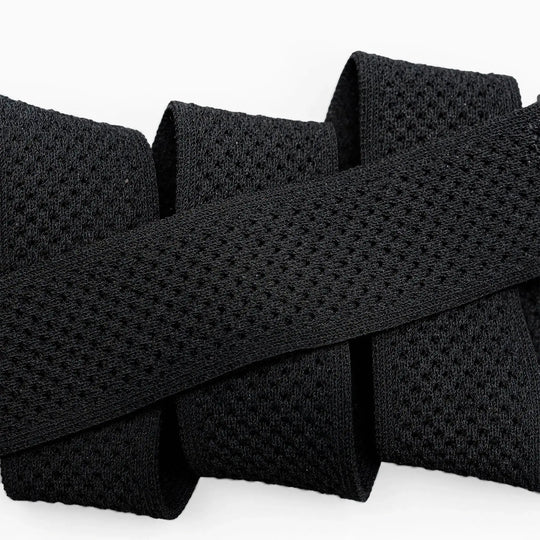 Close-up of the black Momentum elastic stretch belt by Arcade Belts, featuring a mesh-like texture and folded in a zigzag shape against a white background.