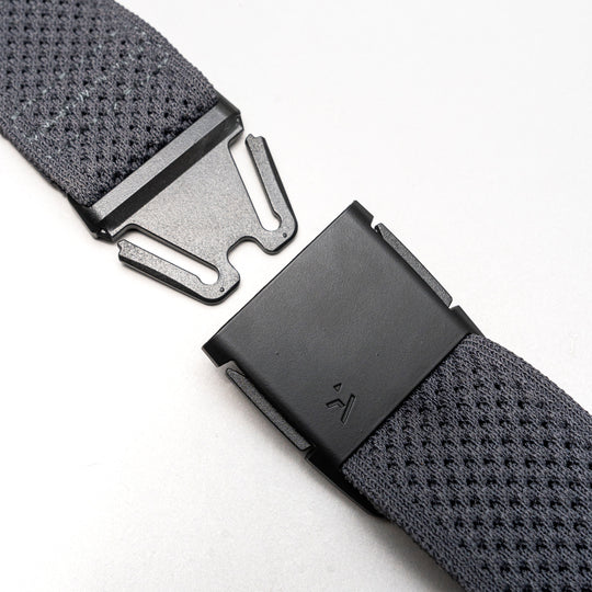 Close-up of the Arcade Belts Momentums black metal buckle on a textured gray strap, featuring a partially open, geometric modern design inspired by low-profile belt styles, set against a plain light background.