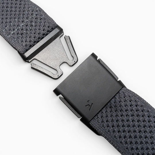 Close-up of the Arcade Belts Momentums black metal buckle on a textured gray strap, featuring a partially open, geometric modern design inspired by low-profile belt styles, set against a plain light background.