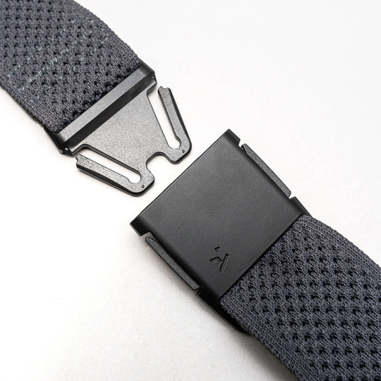 Close-up of the Arcade Belts Momentums black metal buckle on a textured gray strap, featuring a partially open, geometric modern design inspired by low-profile belt styles, set against a plain light background.