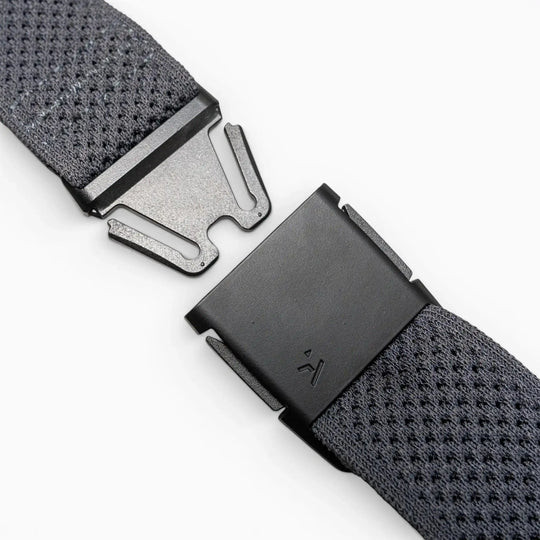 Close-up of the Arcade Belts Momentums black metal buckle on a textured gray strap, featuring a partially open, geometric modern design inspired by low-profile belt styles, set against a plain light background.
