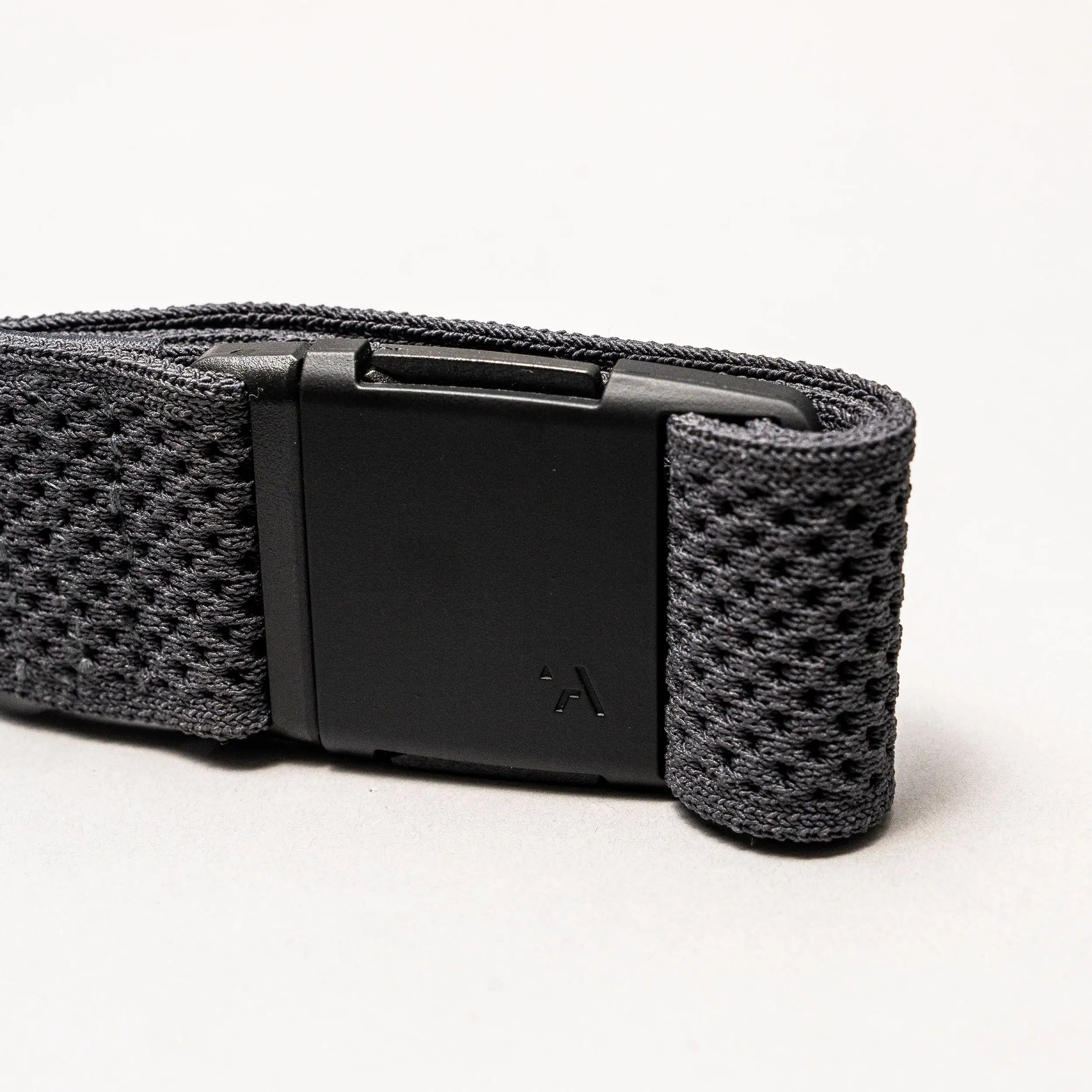 A close-up of the Arcade Belts Momentum strap shows its black textured fabric and rectangular black plastic buckle on a light grey background, highlighting its signature low-profile design.