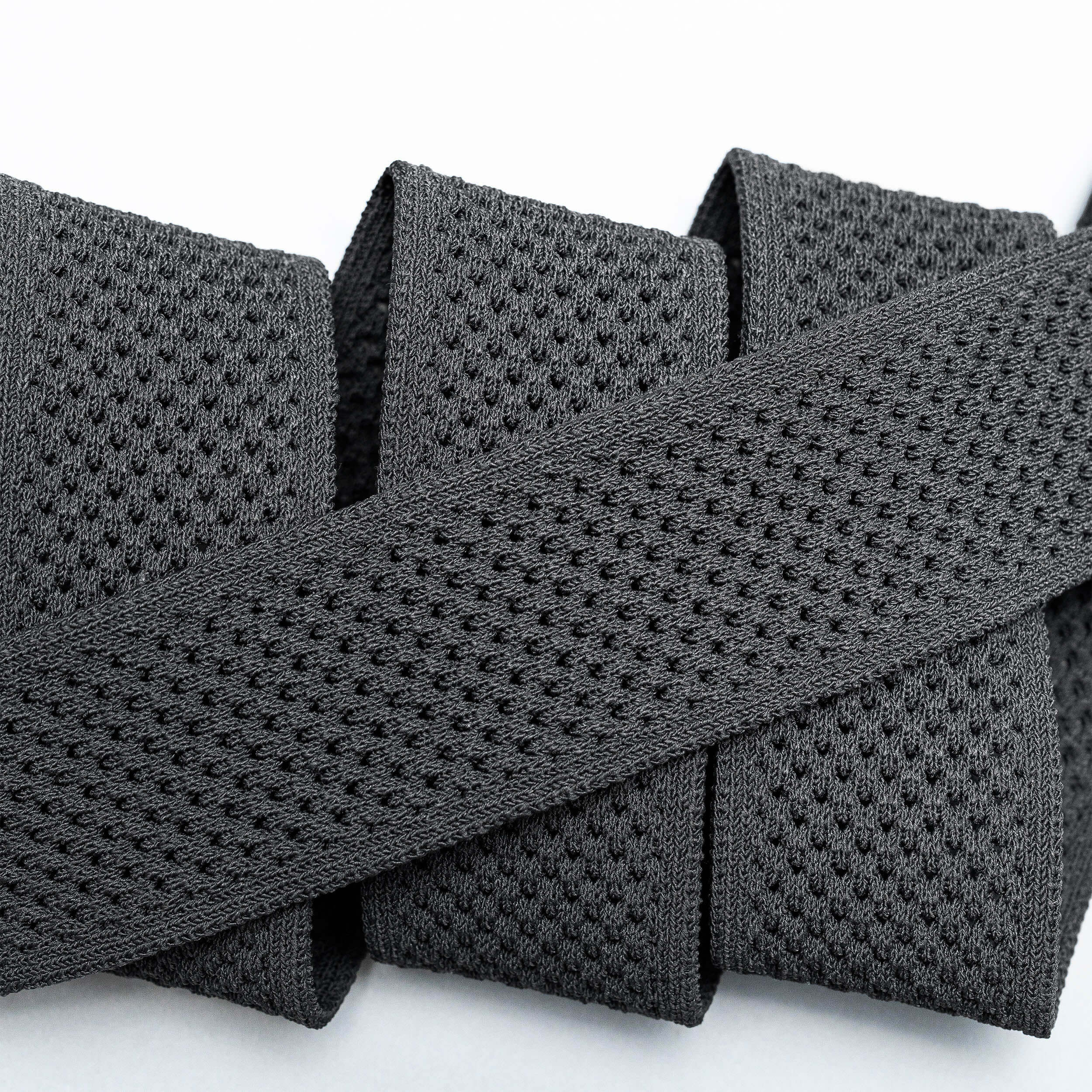 A close-up of the Arcade Belts Momentum: a thick, black elastic band with malleable, perforated webbing, coiled neatly on a white surface for comfort.