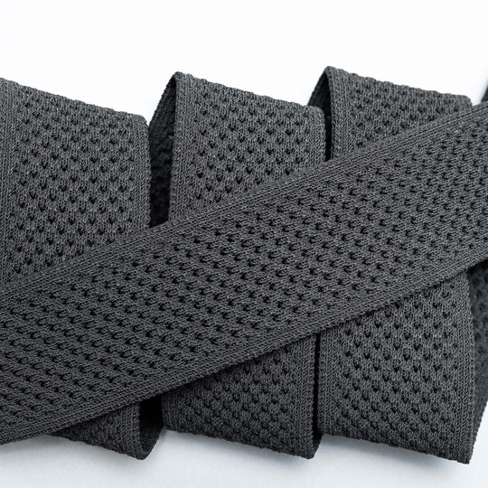 A close-up of the Arcade Belts Momentum: a thick, black elastic band with malleable, perforated webbing, coiled neatly on a white surface for comfort.