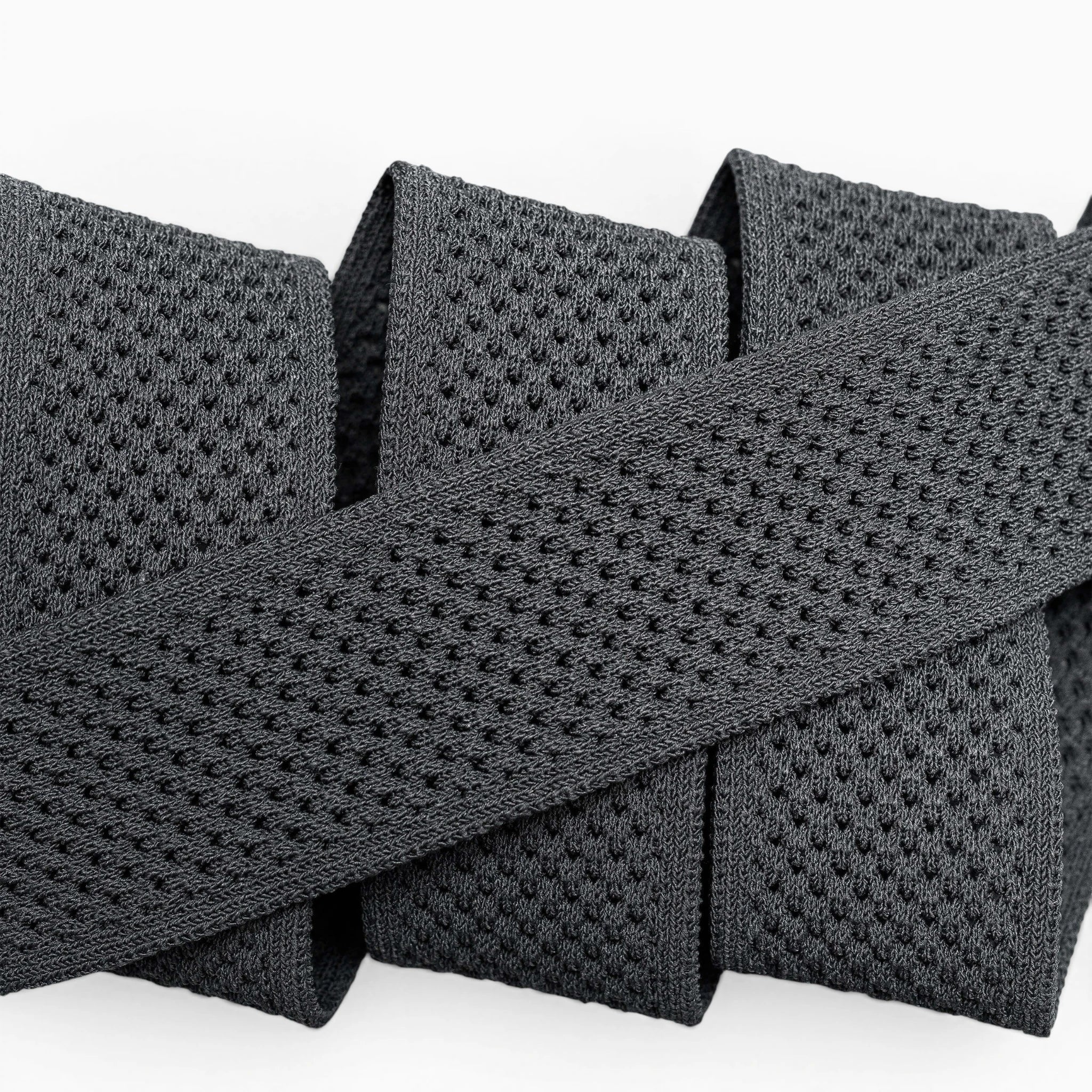 A close-up of the Arcade Belts Momentum: a thick, black elastic band with malleable, perforated webbing, coiled neatly on a white surface for comfort.