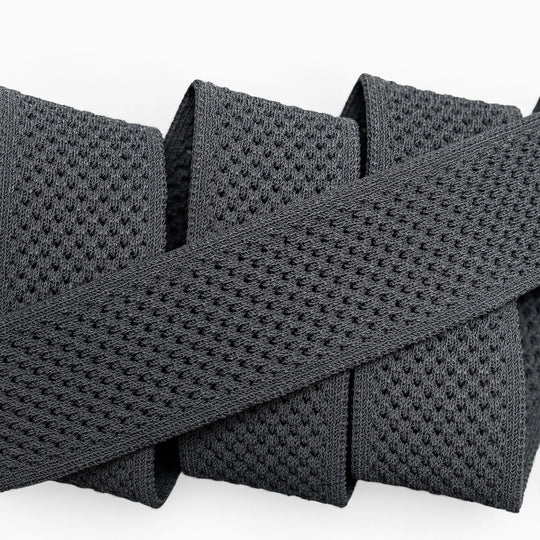 A close-up of the Arcade Belts Momentum: a thick, black elastic band with malleable, perforated webbing, coiled neatly on a white surface for comfort.