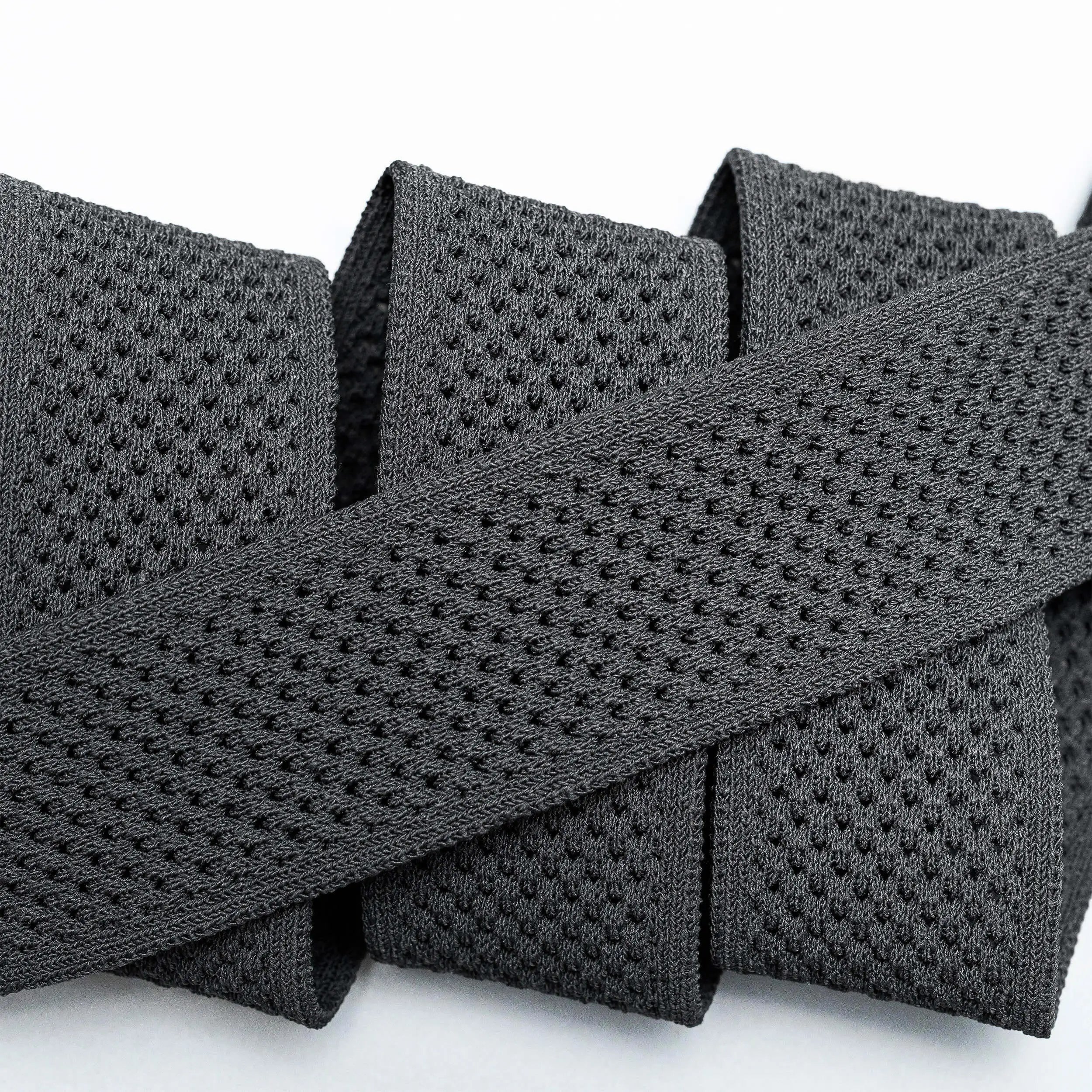 A close-up of the Arcade Belts Momentum: a thick, black elastic band with malleable, perforated webbing, coiled neatly on a white surface for comfort.