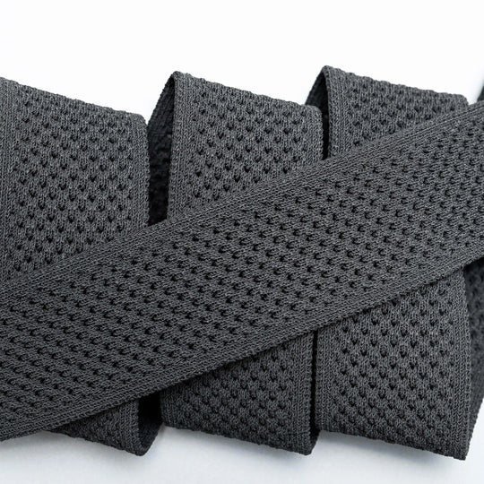 A close-up of the Arcade Belts Momentum: a thick, black elastic band with malleable, perforated webbing, coiled neatly on a white surface for comfort.