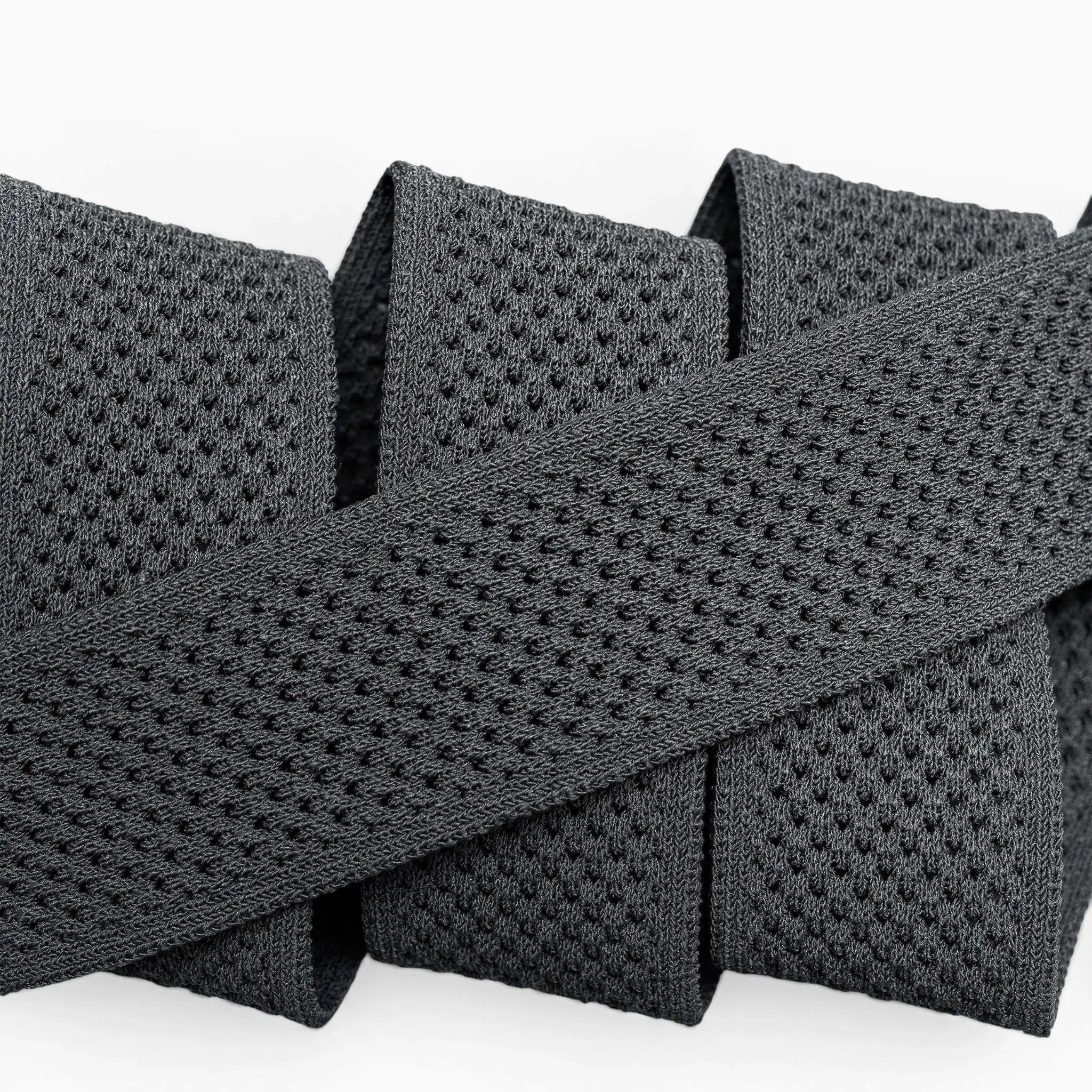 A close-up of the Arcade Belts Momentum: a thick, black elastic band with malleable, perforated webbing, coiled neatly on a white surface for comfort.