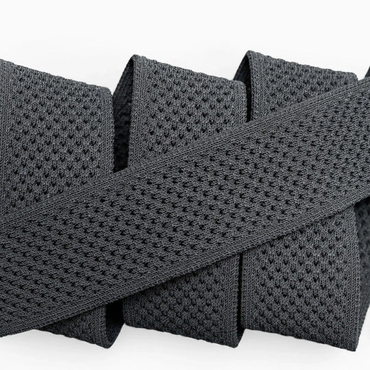A close-up of the Arcade Belts Momentum: a thick, black elastic band with malleable, perforated webbing, coiled neatly on a white surface for comfort.