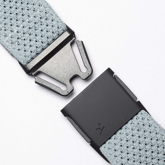 Close-up of the Arcade Belts Momentum: a grey stretch webbing belt with a black metal quick-release buckle shown apart on a white background, illustrating its modern style and secure fastening.