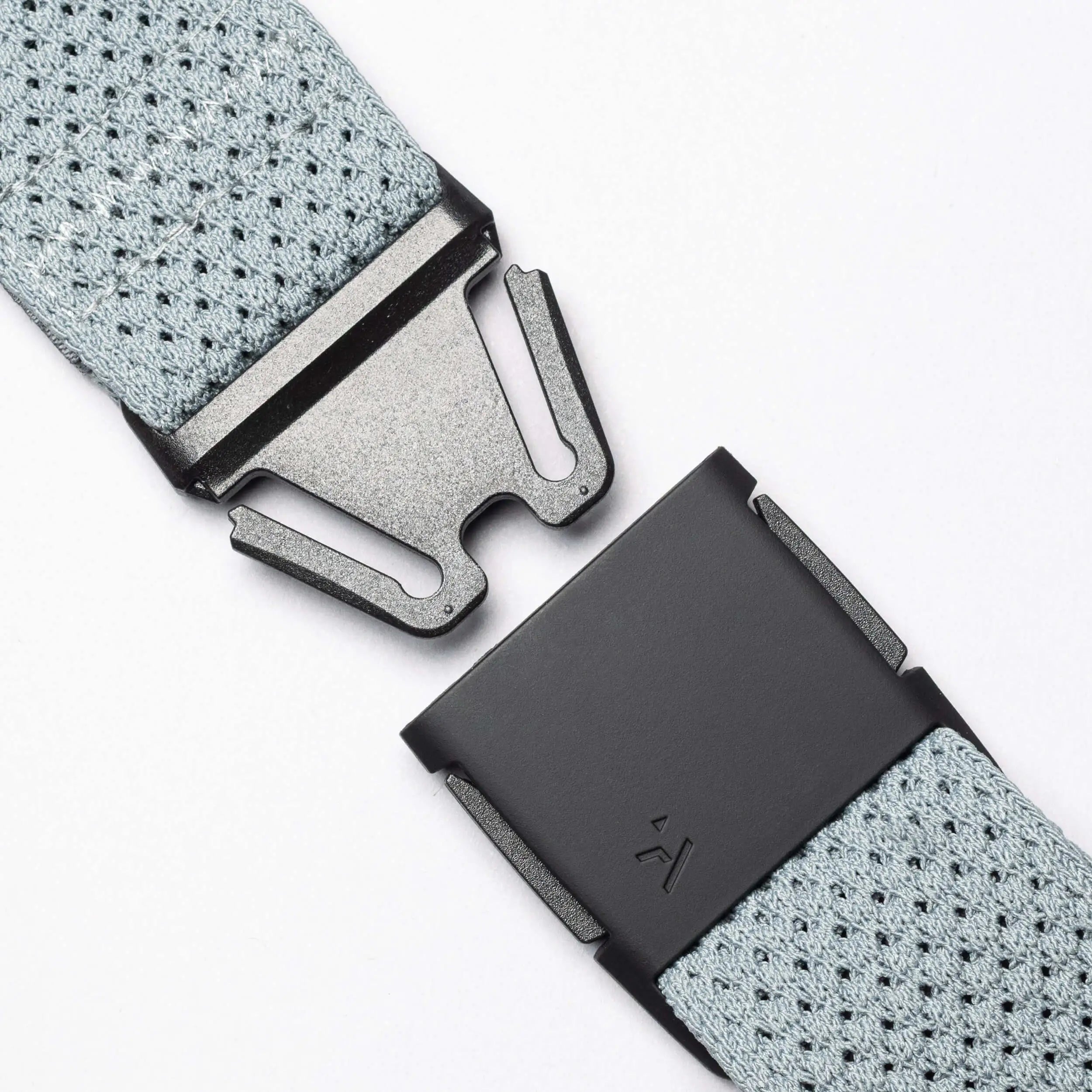 Close-up of the Arcade Belts Momentum: a grey stretch webbing belt with a black metal quick-release buckle shown apart on a white background, illustrating its modern style and secure fastening.