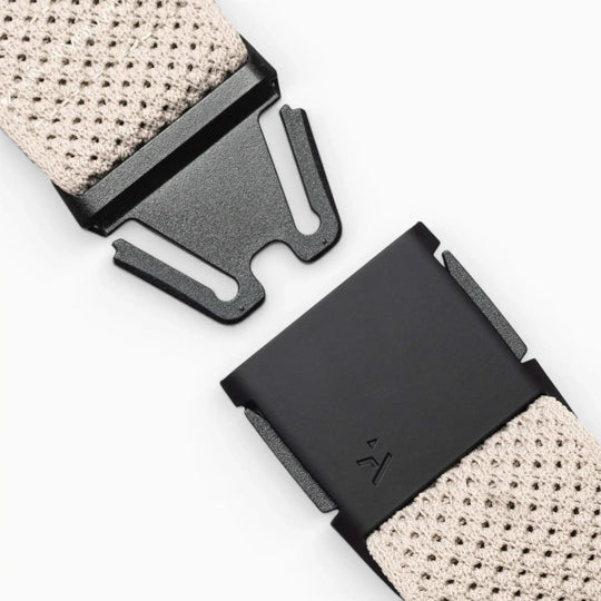 Close-up of the Arcade Belts Momentum: a black metal buckle with a modern geometric design on a beige textured strap—ideal for travel or low-profile wear—set against a neutral background.