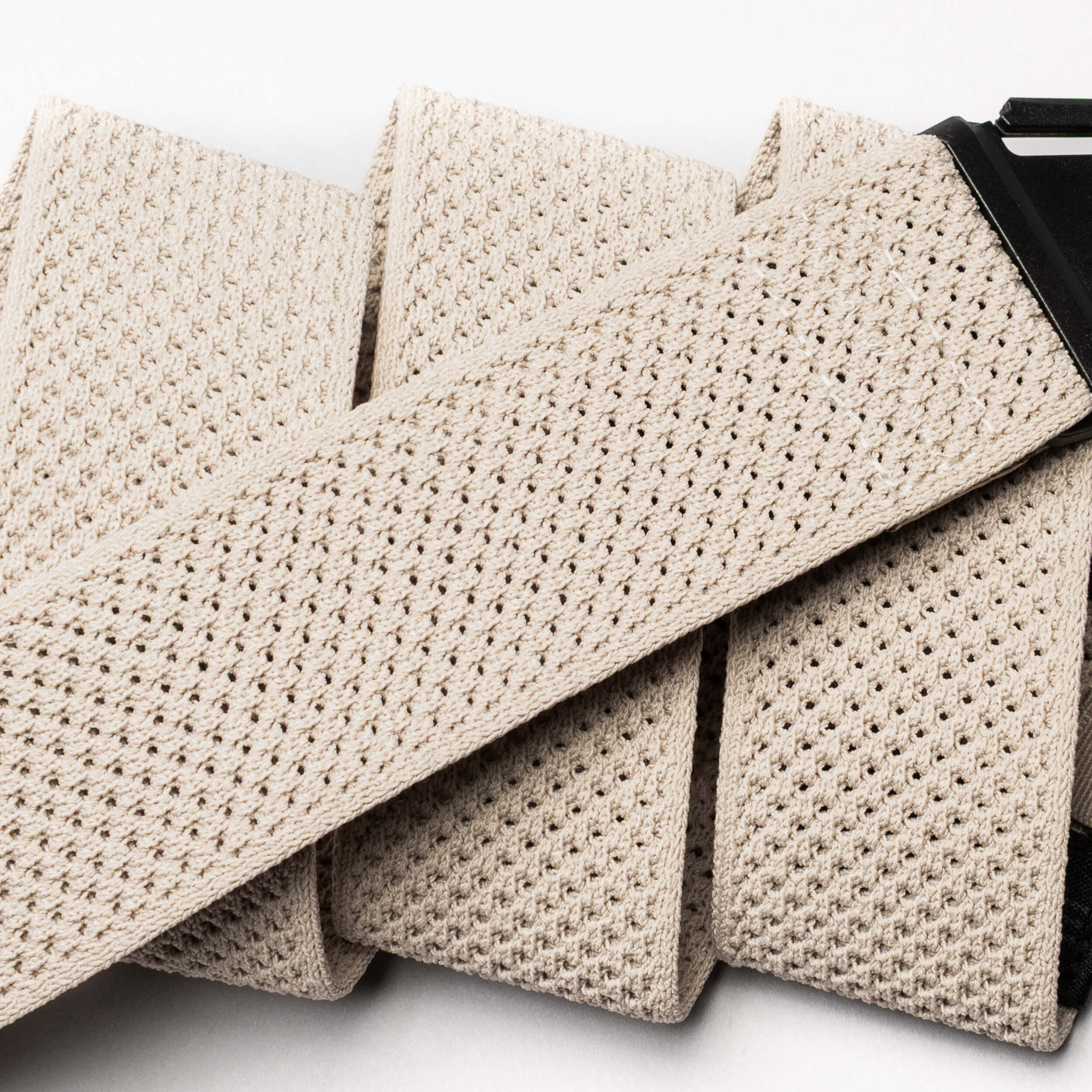 Close-up of the Arcade Belts Momentum in beige, featuring a textured woven and perforated mesh design with a black buckle. This low-profile, comfortable stretch belt is shown against a white background.