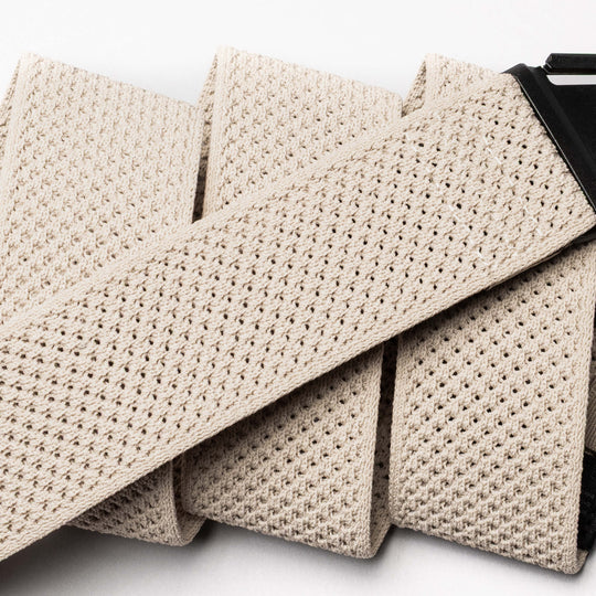 Close-up of the Arcade Belts Momentum in beige, featuring a textured woven and perforated mesh design with a black buckle. This low-profile, comfortable stretch belt is shown against a white background.