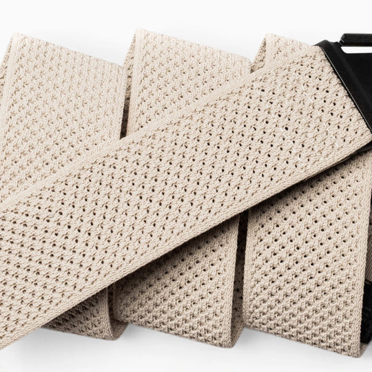 Close-up of the Arcade Belts Momentum in beige, featuring a textured woven and perforated mesh design with a black buckle. This low-profile, comfortable stretch belt is shown against a white background.