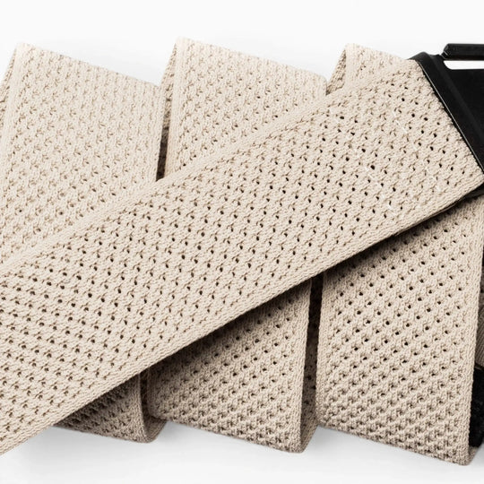 Close-up of the Arcade Belts Momentum in beige, featuring a textured woven and perforated mesh design with a black buckle. This low-profile, comfortable stretch belt is shown against a white background.