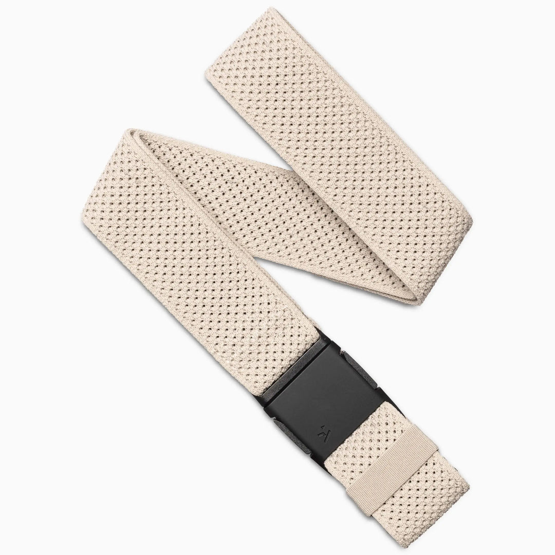 The Momentum by Arcade Belts is a beige woven elastic stretch belt with a textured pattern and black rectangular buckle, shown laid flat with the end tucked under—ideal as a low-profile belt for daily wear or travel.