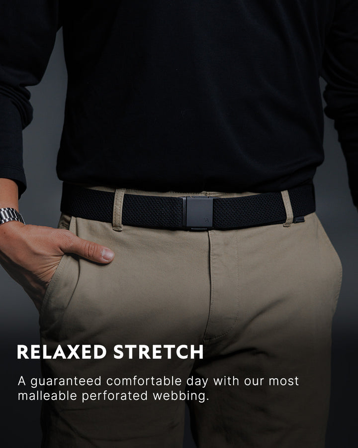 A person wearing khaki pants, a black stretch travel belt with a plastic buckle, and a black long-sleeve shirt. Text reads: RELAXED STRETCH. Enjoy all-day comfort from our most malleable perforated webbing.
