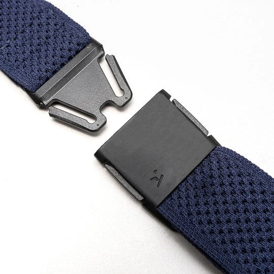 Close-up of the Arcade Belts Momentum stretch webbing strap in navy blue, featuring a black plastic clasp thats partly unfastened, shown on a light gray background.