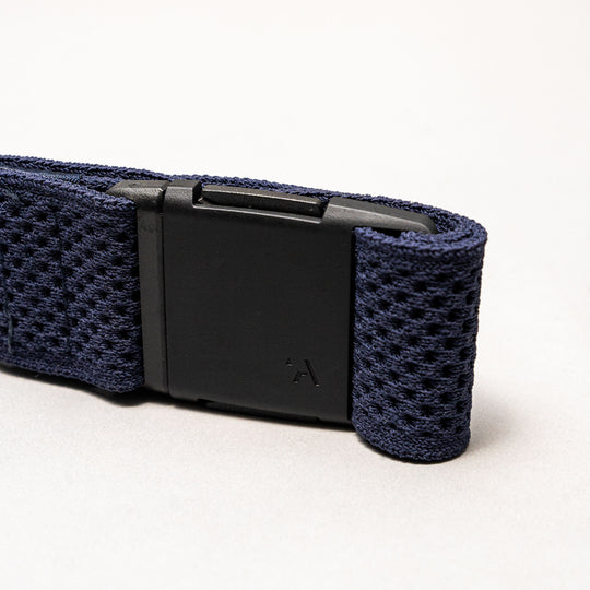 A close-up of the Arcade Belts Momentum, a dark blue elastic stretch belt with a black rectangular plastic buckle, set against a plain light gray background.